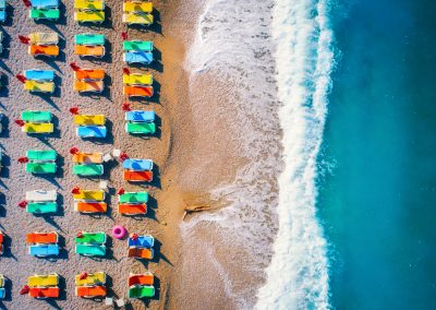 Aerial view of lying woman on the sandy beach with colorful chaise-lounges. Young woman on the sea at sunset in Europe. Top view. Landscape with girl on the seashore, blue water and waves. Resort